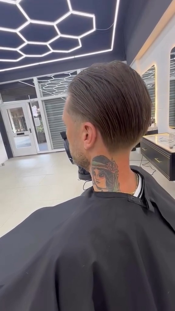 Achterhoofd van een klant met een slick back en een fade, onder het honingraatplafond